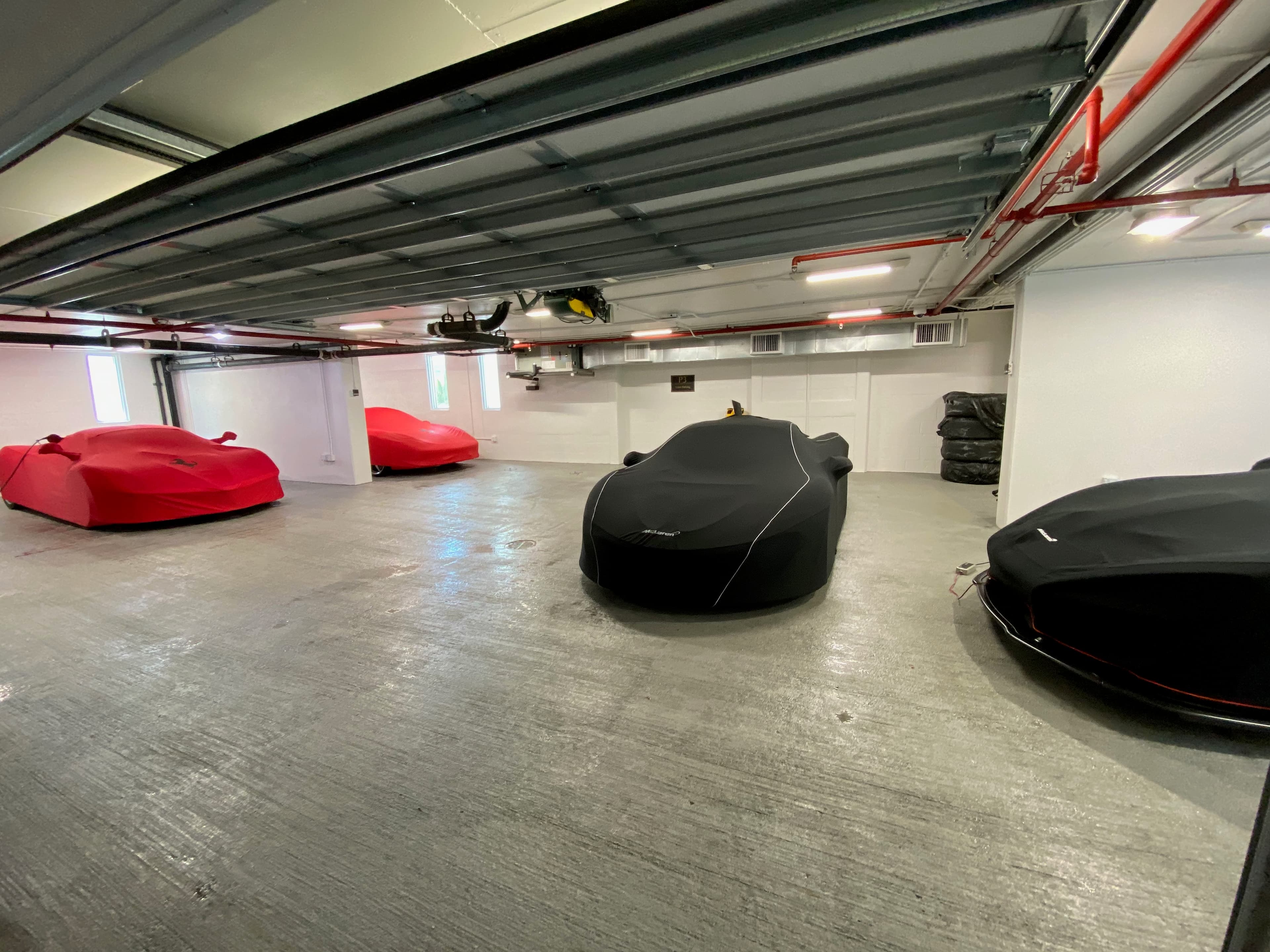 Climate-controlled supercar storage — covered Ferraris and a McLaren under fitted indoor covers