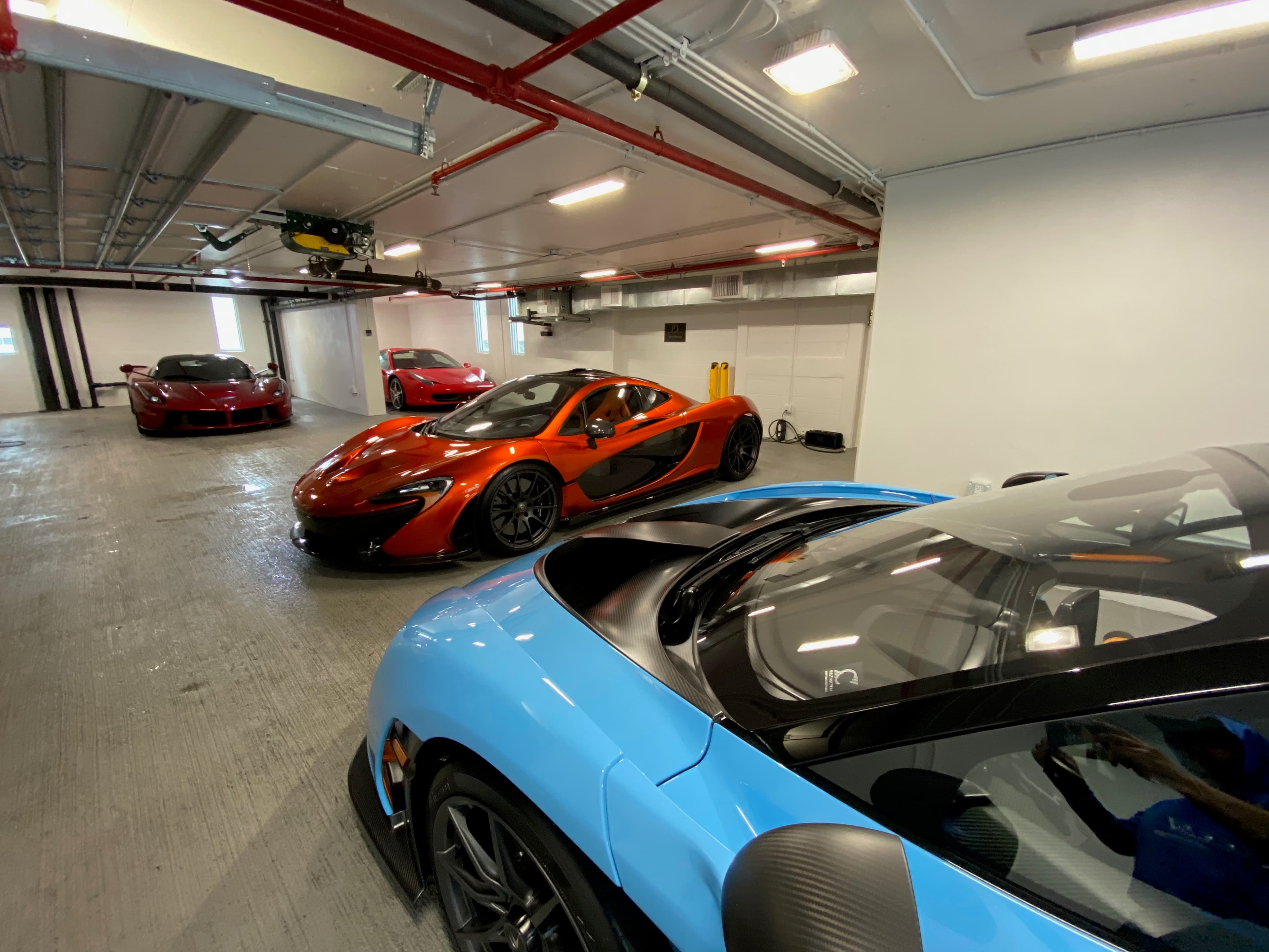 Hypercar collection in private storage — Ferrari LaFerrari, orange McLaren P1, and a baby blue McLaren parked side by side