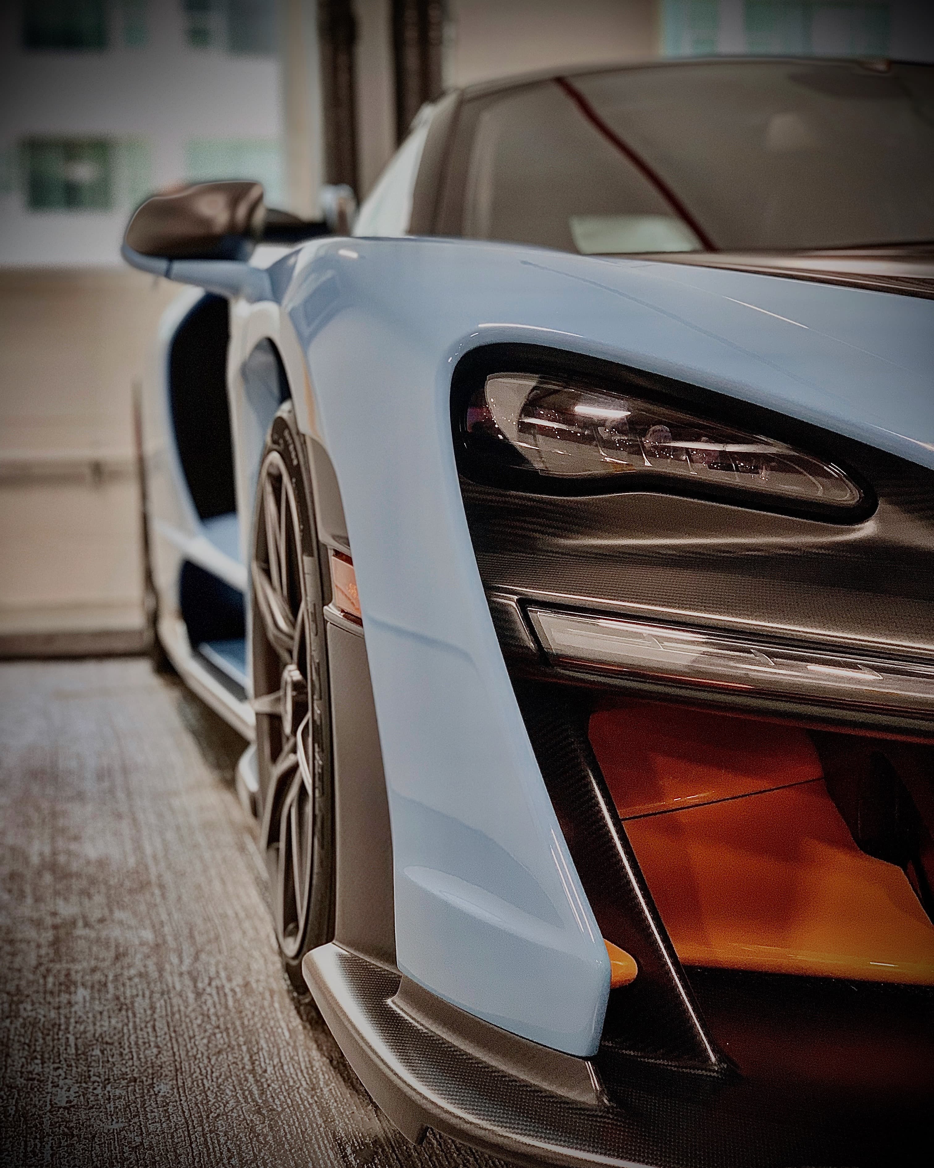 Close-up of a baby blue McLaren Senna headlight, carbon fiber front splitter, and forged wheel