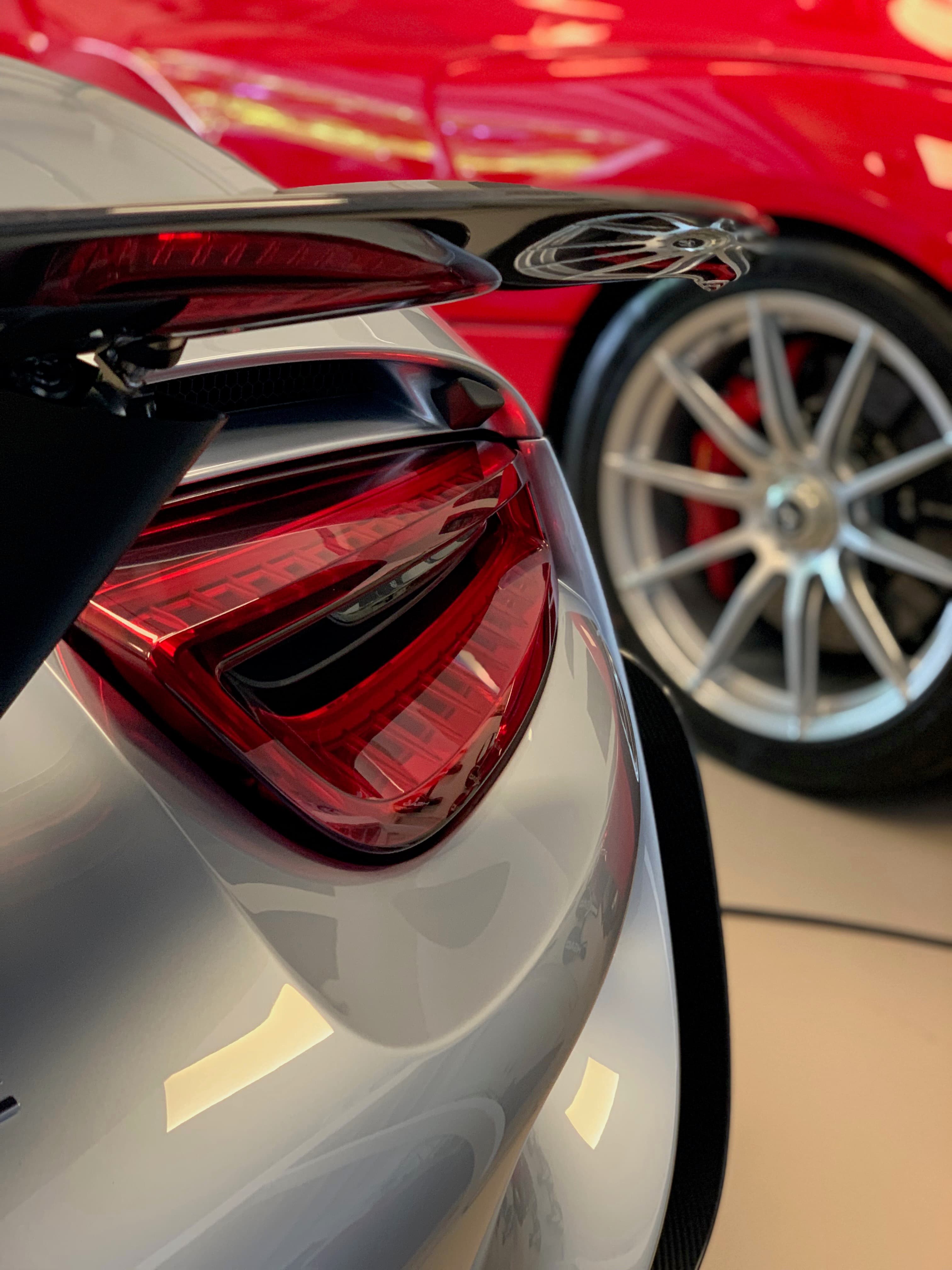 Close-up of a silver Porsche rear spoiler and taillight with a red exotic reflected in the freshly polished paint